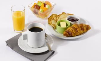 a breakfast table with a cup of coffee , croissants , fruit , and a glass of orange juice at Campanile Paris Est - Bobigny