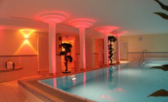 a large swimming pool with a red and white light installation , surrounded by columns and walls at Hotel Sonnenblick