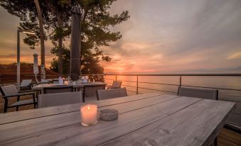 a wooden table with a lit candle on it , overlooking the ocean and trees at sunset at Poseidon Hotel