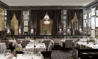 a large dining room with multiple tables and chairs , a chandelier hanging from the ceiling , and purple curtains at Hotel d'Angleterre