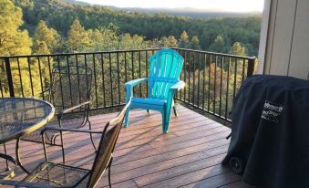 a wooden deck overlooking a forest , with a blue chair and a table on the deck at Three Pines