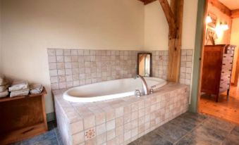 a large , round bathtub is situated in a room with white tiles and wooden beams at Blueberry Hill Inn