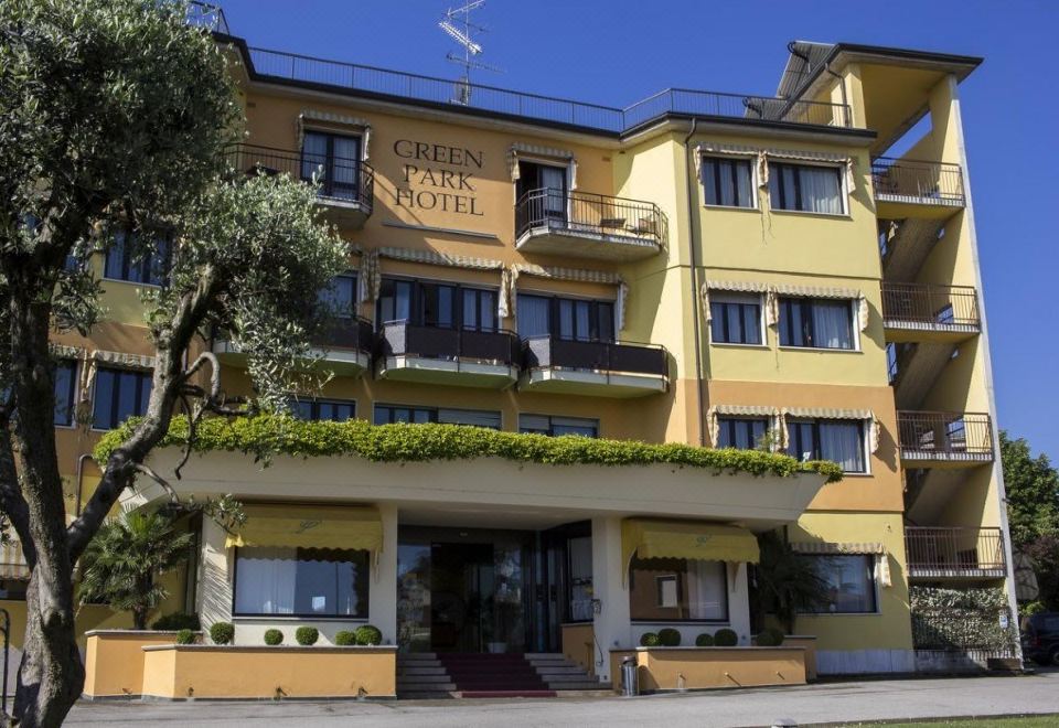 a large hotel building with multiple balconies and windows , situated on a street with trees and a clear blue sky at Green Park Hotel