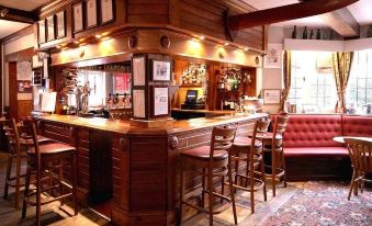 a well - decorated bar with wooden furniture , including a long bar counter and several stools , surrounded by comfortable seating at The Baskerville