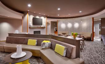 a modern , well - lit living room with multiple couches and chairs arranged around a dining table at SpringHill Suites Thatcher