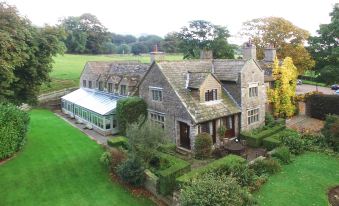 aerial view of a large stone house surrounded by green grass and trees , with a tennis court in the background at Stone House Hotel