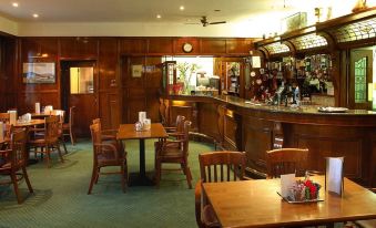 a dining room with a wooden table , chairs , and a bar in the background at Londonderry Arms Hotel