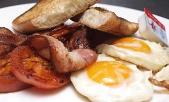 a plate of breakfast food , consisting of eggs , bacon , toast , and tomatoes , is placed on a dining table at Morphettville Motor Inn