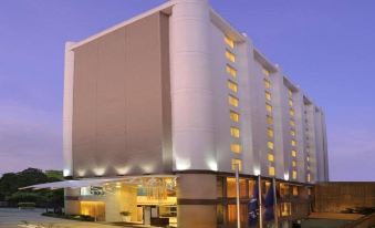 a modern building with a large white column and many windows , located on a street at Four Points by Sheraton Ahmedabad