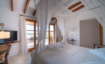 The bedroom is furnished with a white bed and has large windows that overlook the pool area at Petit Hotel Forn NOU