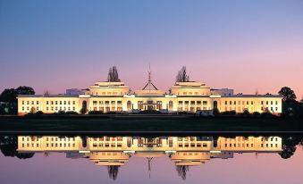 a large white building , possibly the parliament house , is reflected in a body of water at Golden Age Motor Inn