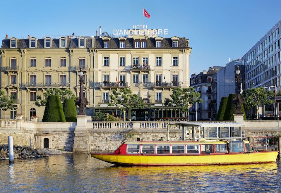 a large building with a red flag on top and a yellow boat in the water at Hotel d'Angleterre