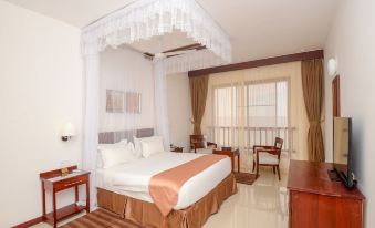 a large bed with a white and orange color scheme is in the middle of a room with a desk , chair , and window at Raphael's Hotel