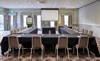 a conference room with a projector screen , chairs , and tables set up for a meeting at Holiday Inn Leeds - Garforth