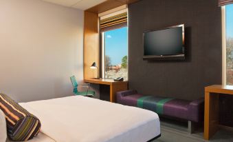 a modern hotel room with a large window , purple couch , bed , and flat screen tv at Aloft Chesapeake