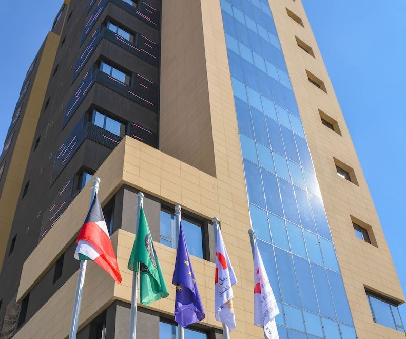 a tall building with a blue and beige color scheme , surrounded by multiple flags of different countries at Swiss-Belboutique Bneid Al Gar Kuwait