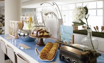 a table with various desserts , including waffles and waffles on toast , next to a window with flowers at Novotel Marne-la-Vallée Noisy-Le-Grand