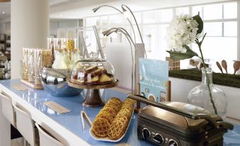 a table with various desserts , including waffles and waffles on toast , next to a window with flowers at Novotel Marne la Vallee Noisy le Grand Hotel