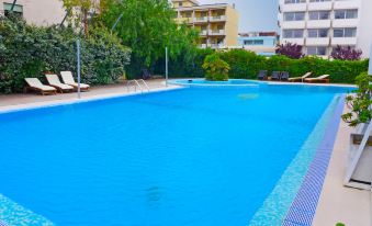 a large , rectangular swimming pool with blue water and white tiles , surrounded by lounge chairs and trees , in front of a building with multiple bal at Nautilus