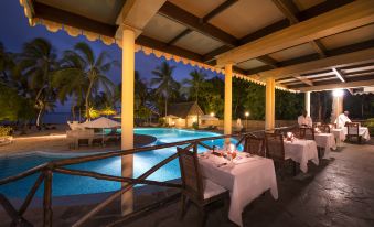 an outdoor dining area with a table set for dinner , surrounded by palm trees and a swimming pool at Diamonds Dream of Africa