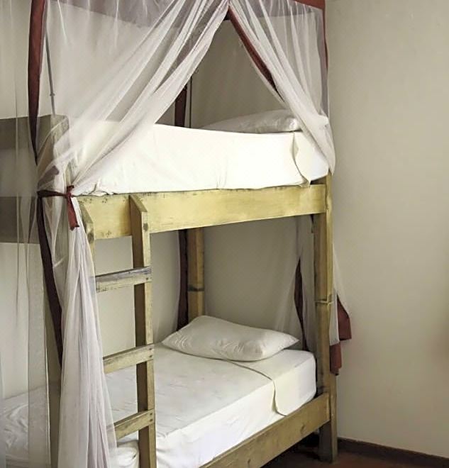 a wooden bunk bed with a white sheet and pillow on the bottom bed , surrounded by white curtains at Fawlty Towers Guest House