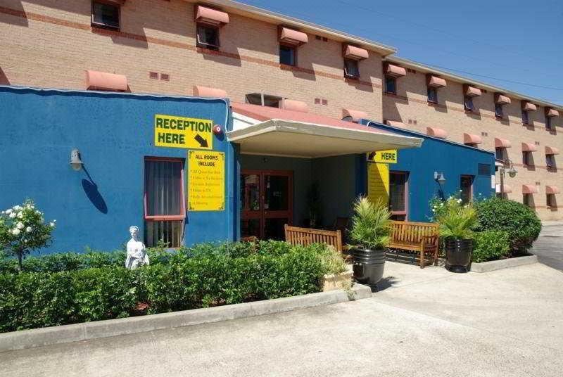 "a blue building with a sign that reads "" reception here "" and a bench in front of it" at Arena Hotel (Formerly Sleep Express Motel)