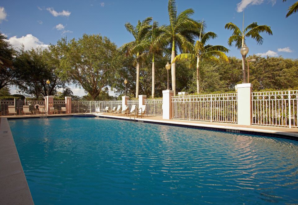 a swimming pool surrounded by palm trees , with several lounge chairs placed around it for relaxation at DoubleTree by Hilton Sunrise - Sawgrass Mills