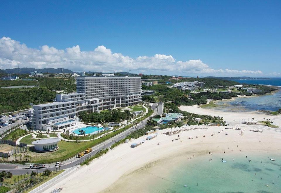 a large hotel on the beach , surrounded by lush greenery and clear blue water , with a white sandy beach nearby at The Orion Hotel Motobu Resort & Spa