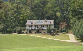 a large white house situated on a grassy hill , surrounded by trees and a lush green field at Mountain Cove Farms Resort