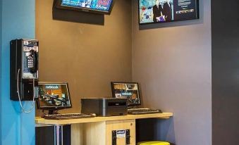 a modern office space with blue walls , a wooden desk , two computer monitors , and yellow stools at Ibis Budget Brisbane Airport