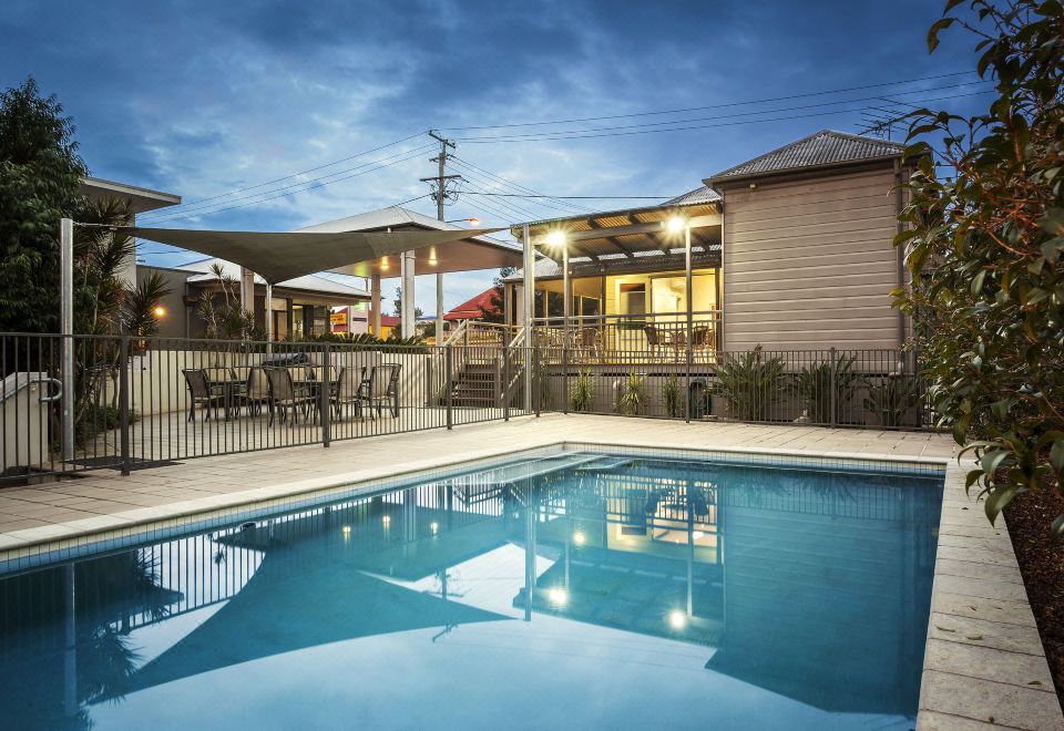 a large swimming pool is surrounded by a patio and tables , with buildings in the background at Quest Ipswich