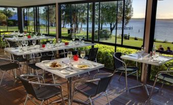 an outdoor dining area with several tables and chairs , where people are enjoying a meal at BreakFree Raffertys Beach Resort