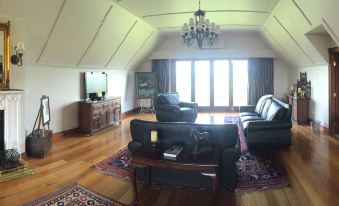 a spacious living room with hardwood floors , a large flat - screen tv mounted on the wall , and a dining table in the corner at Lake Karapiro Lodge