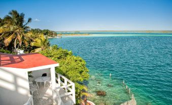 a beautiful beach scene with a red - roofed building overlooks the ocean and a white fence at Hotel Laguna Bacalar