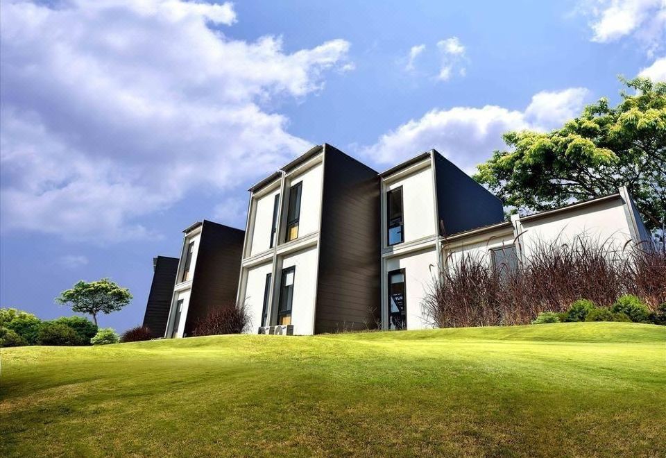 a modern , white building with black and brown accents is surrounded by a green lawn and trees at Lakeview Terrace Resort Pengerang