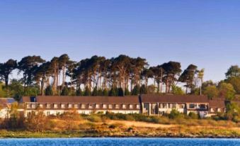 a large building with a brown roof is surrounded by trees and overlooks a calm blue lake at Isle of Mull Hotel and Spa