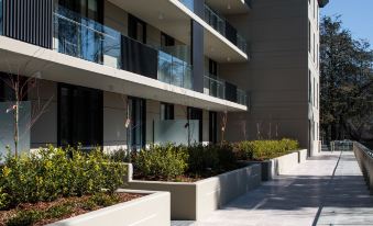 a modern apartment building with balconies and greenery , surrounded by a well - maintained walkway and flower beds at Knightsbridge Canberra