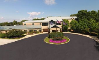 a large building with a circular flower arrangement in front , surrounded by trees and a parking lot at Desmond Hotel Malvern, a DoubleTree by Hilton