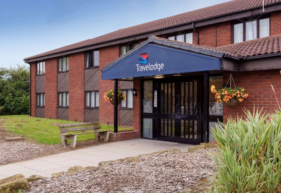 an exterior view of a travelodge hotel with a brick building , flower pots , and a sign above the entrance at Travelodge Hull South Cave