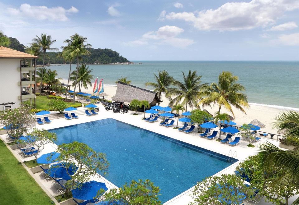 a large swimming pool is surrounded by blue lounge chairs and umbrellas , with palm trees in the background at Hyatt Regency Kuantan Resort