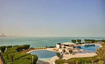 a large swimming pool is surrounded by lush greenery and lounge chairs , with the ocean visible in the background at Marina Hotel