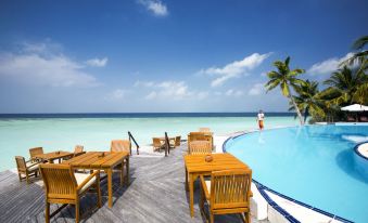 a wooden table and chairs are set up on a deck overlooking a pool and the ocean at Filitheyo Island Resort