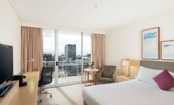 a hotel room with a large bed , two chairs , a desk , and a window overlooking a city view at Sage Hotel Wollongong