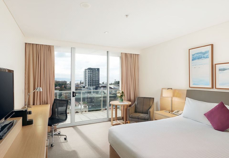 a hotel room with a large bed , two chairs , a desk , and a window overlooking a city view at Sage Hotel Wollongong