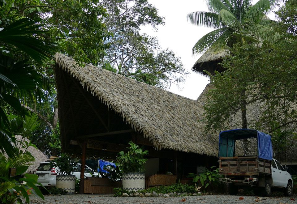 a thatched - roof building surrounded by lush greenery , with a truck parked in front of it at Lapa Rios Lodge by Boena