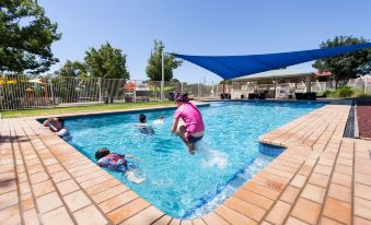 a group of children are playing in a swimming pool , with one person jumping into the water at Nrma Dubbo Holiday Park