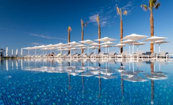 a row of white umbrellas and lounge chairs are lined up in front of a blue pool at Potidea Palace Hotel