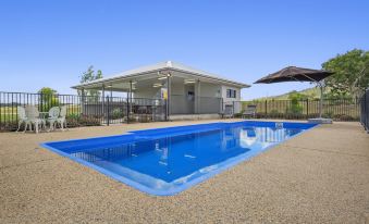 a blue swimming pool surrounded by a grassy area , with a house in the background at Casa Nostra Motel