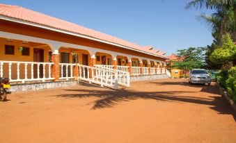 a brick building with a red roof , surrounded by trees and a dirt road , and a white truck parked in front of it at Country Inn Masindi
