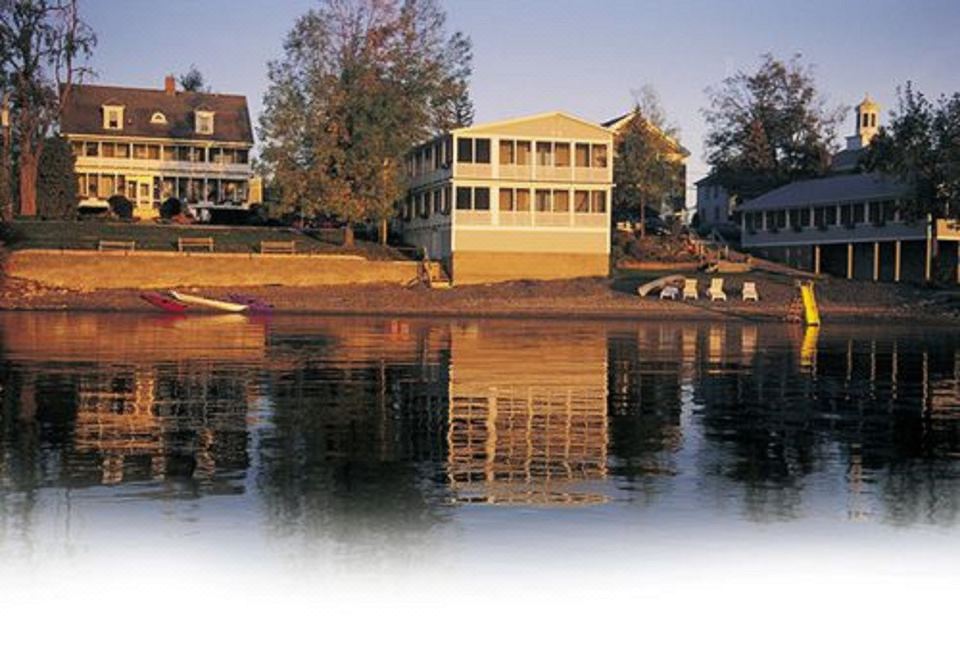 a serene scene of a boat docked on a calm lake , with houses and trees in the background at The North Hero House Inn & Restaurant